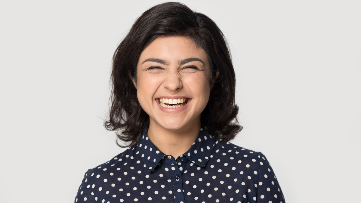 Headshot portrait of excited millennial indian woman isolated on grey studio background look at camera smiling, happy ethnic young female posing feel positive overjoyed, laugh showing white teeth